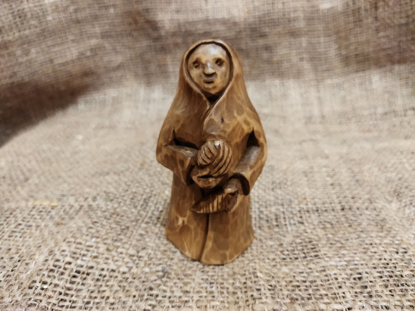 Hand-carved wooden statuette of the Slavic goddess Makosh, depicted with a serene expression, holding symbols of fate and abundance, set against a natural burlap background.