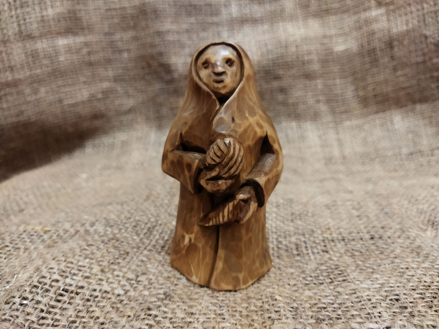 Hand-carved wooden statuette of the Slavic goddess Makosh, depicted with a serene expression, holding symbols of fate and abundance, set against a natural burlap background.