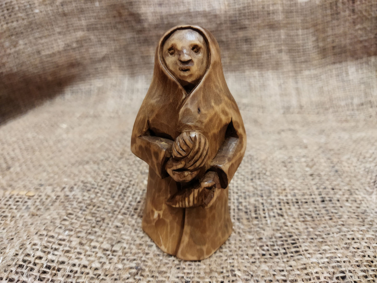 Hand-carved wooden statuette of the Slavic goddess Makosh, depicted with a serene expression, holding symbols of fate and abundance, set against a natural burlap background.