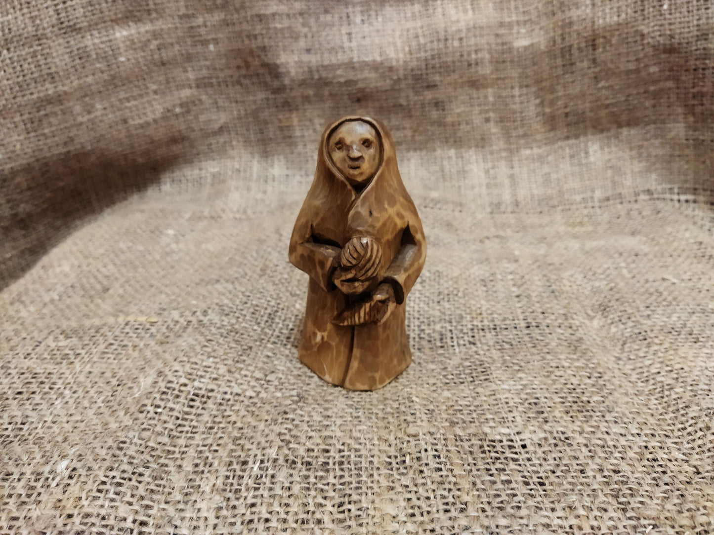 Hand-carved wooden statuette of the Slavic goddess Makosh, depicted with a serene expression, holding symbols of fate and abundance, set against a natural burlap background.