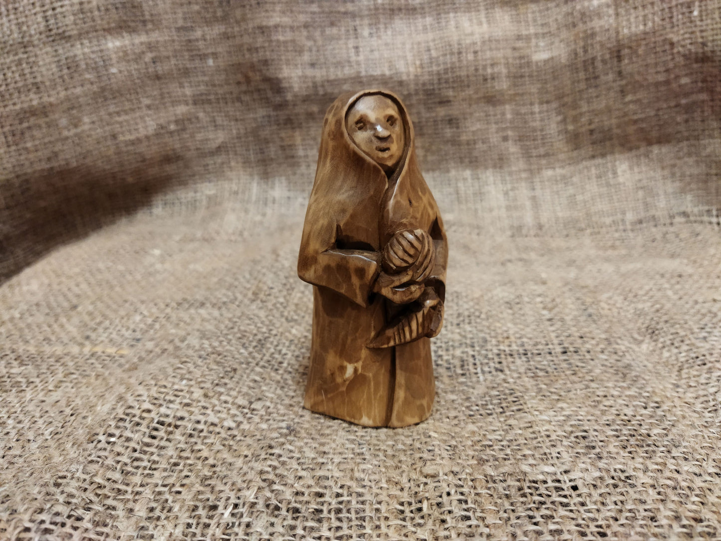 Hand-carved wooden statuette of the Slavic goddess Makosh, depicted with a serene expression, holding symbols of fate and abundance, set against a natural burlap background.