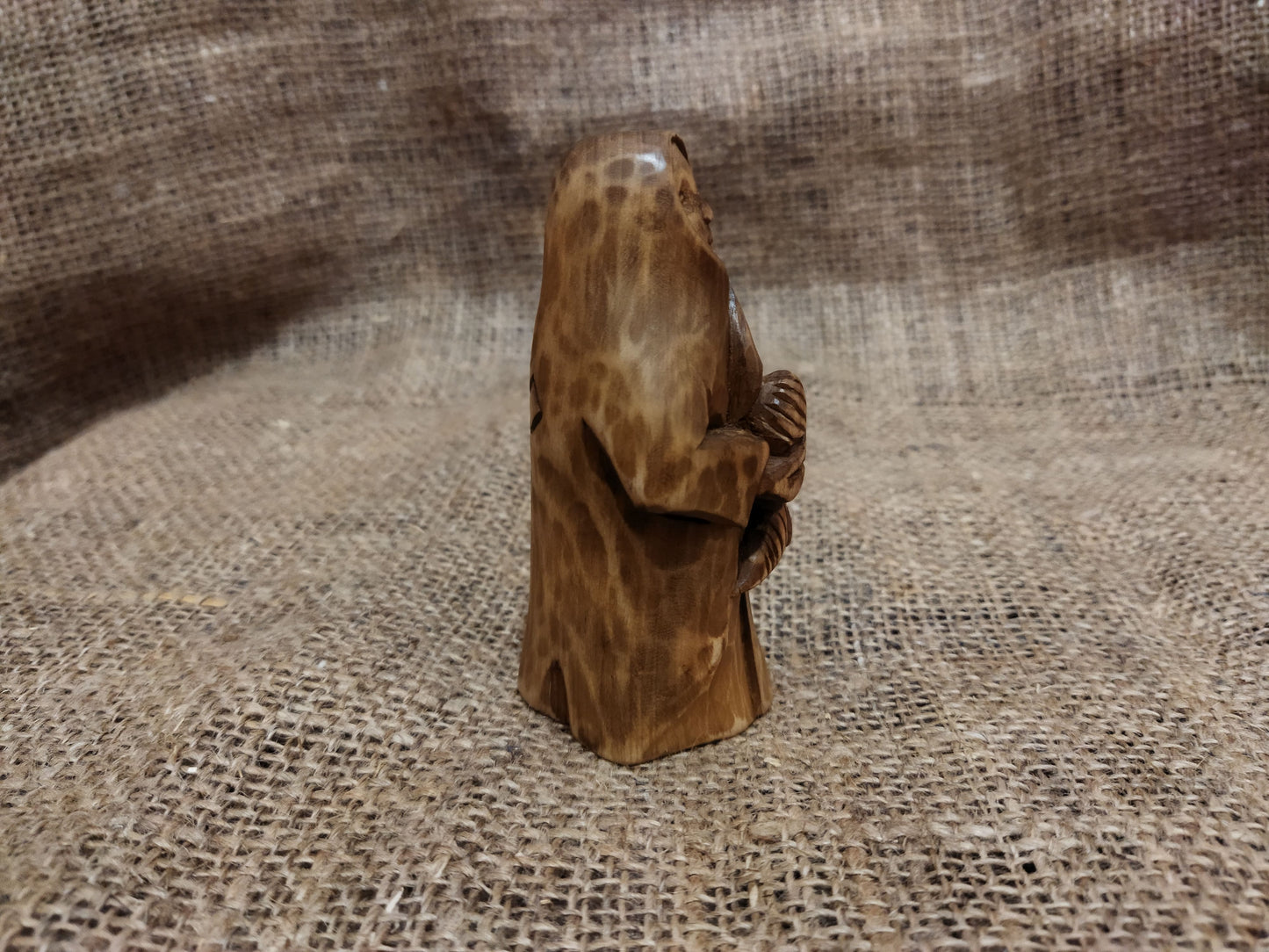 Hand-carved wooden statuette of the Slavic goddess Makosh, depicted with a serene expression, holding symbols of fate and abundance, set against a natural burlap background.