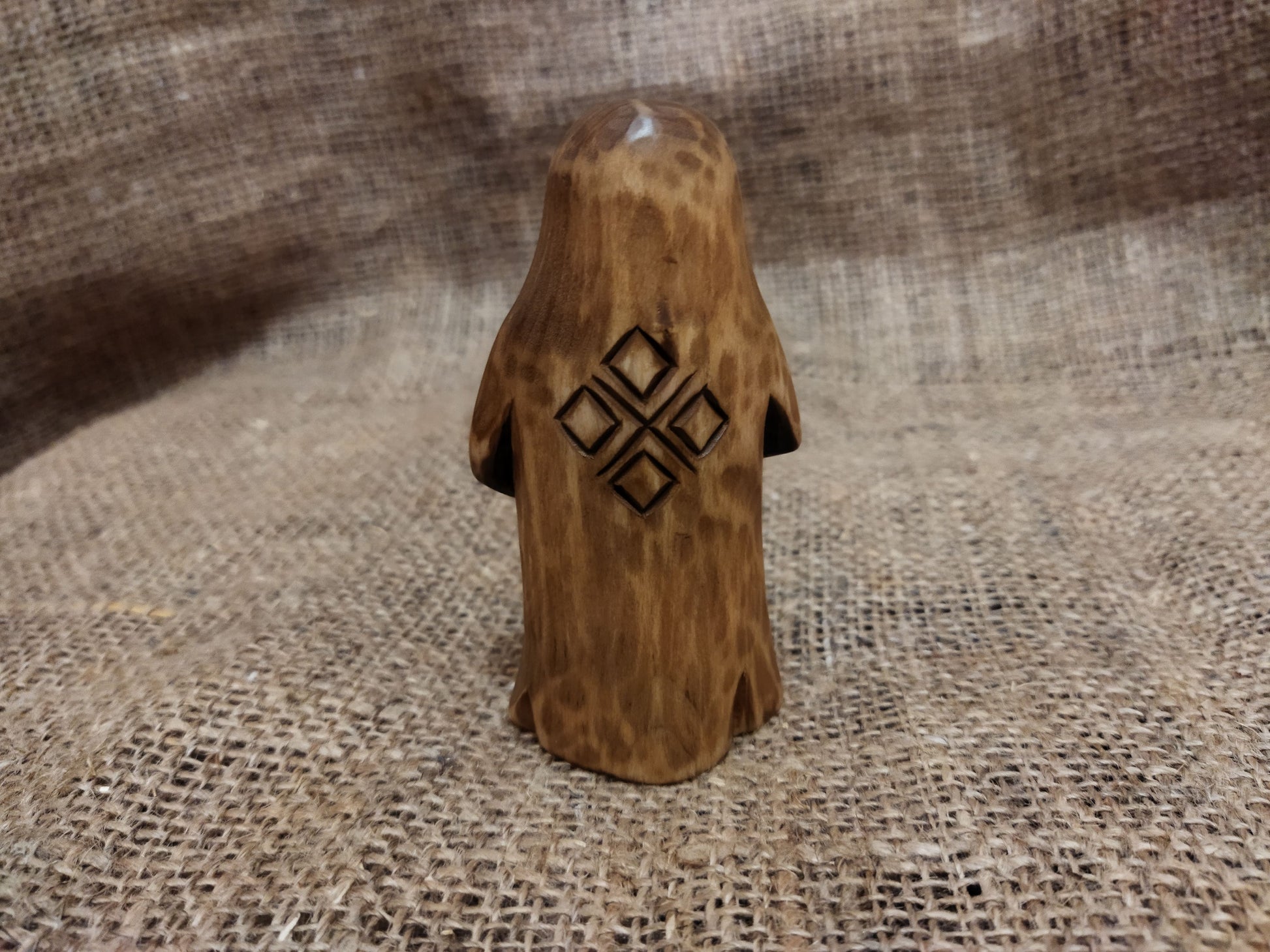 Hand-carved wooden statuette of the Slavic goddess Makosh, depicted with a serene expression, holding symbols of fate and abundance, set against a natural burlap background.