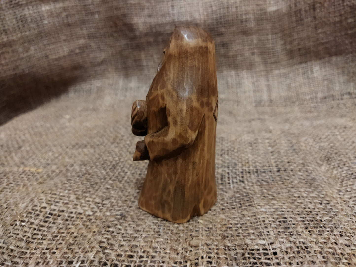 Hand-carved wooden statuette of the Slavic goddess Makosh, depicted with a serene expression, holding symbols of fate and abundance, set against a natural burlap background.