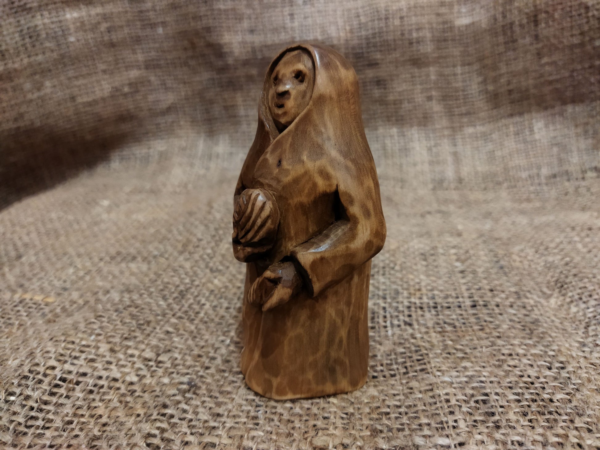 Hand-carved wooden statuette of the Slavic goddess Makosh, depicted with a serene expression, holding symbols of fate and abundance, set against a natural burlap background.