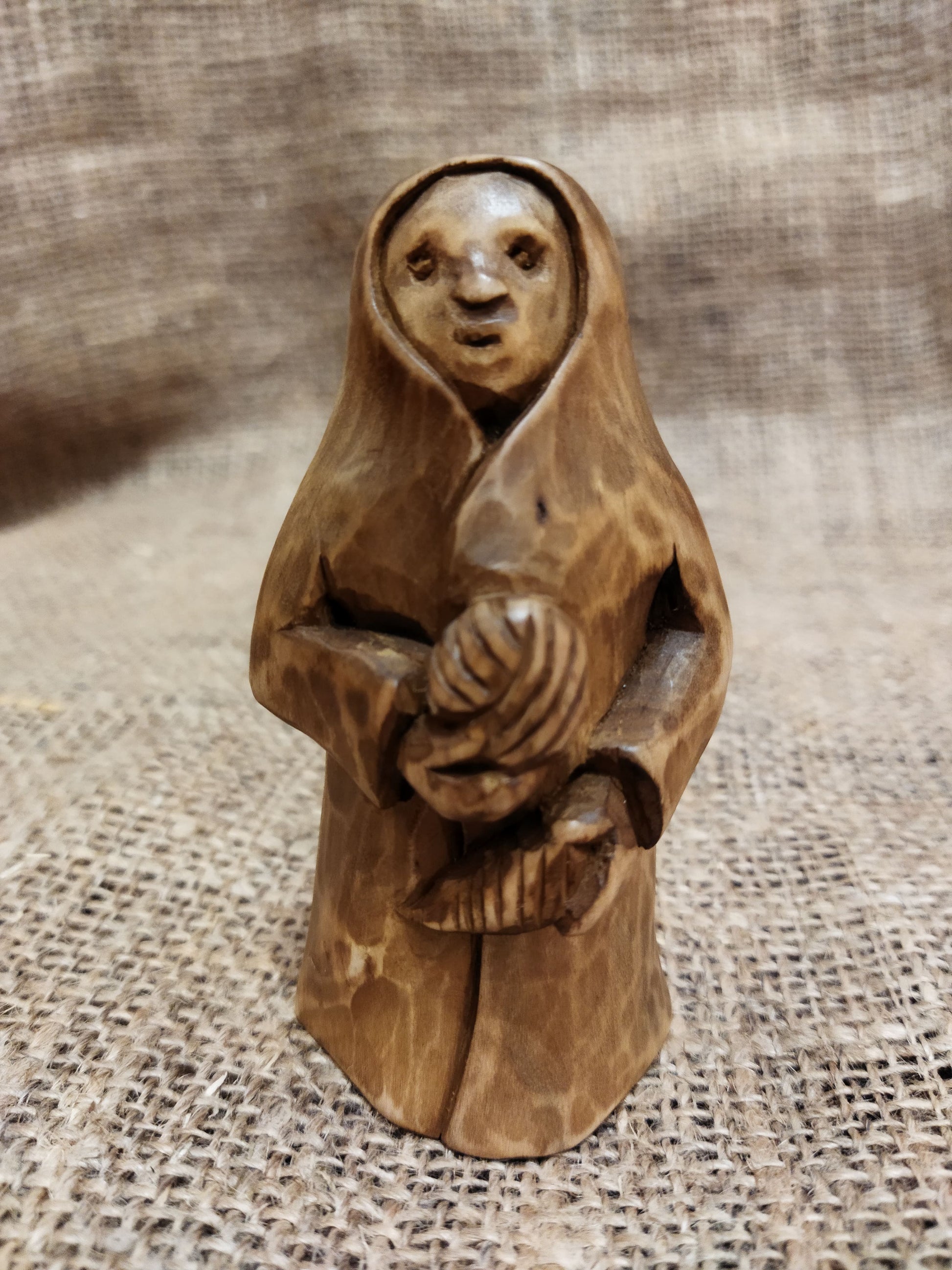 Hand-carved wooden statuette of the Slavic goddess Makosh, depicted with a serene expression, holding symbols of fate and abundance, set against a natural burlap background.