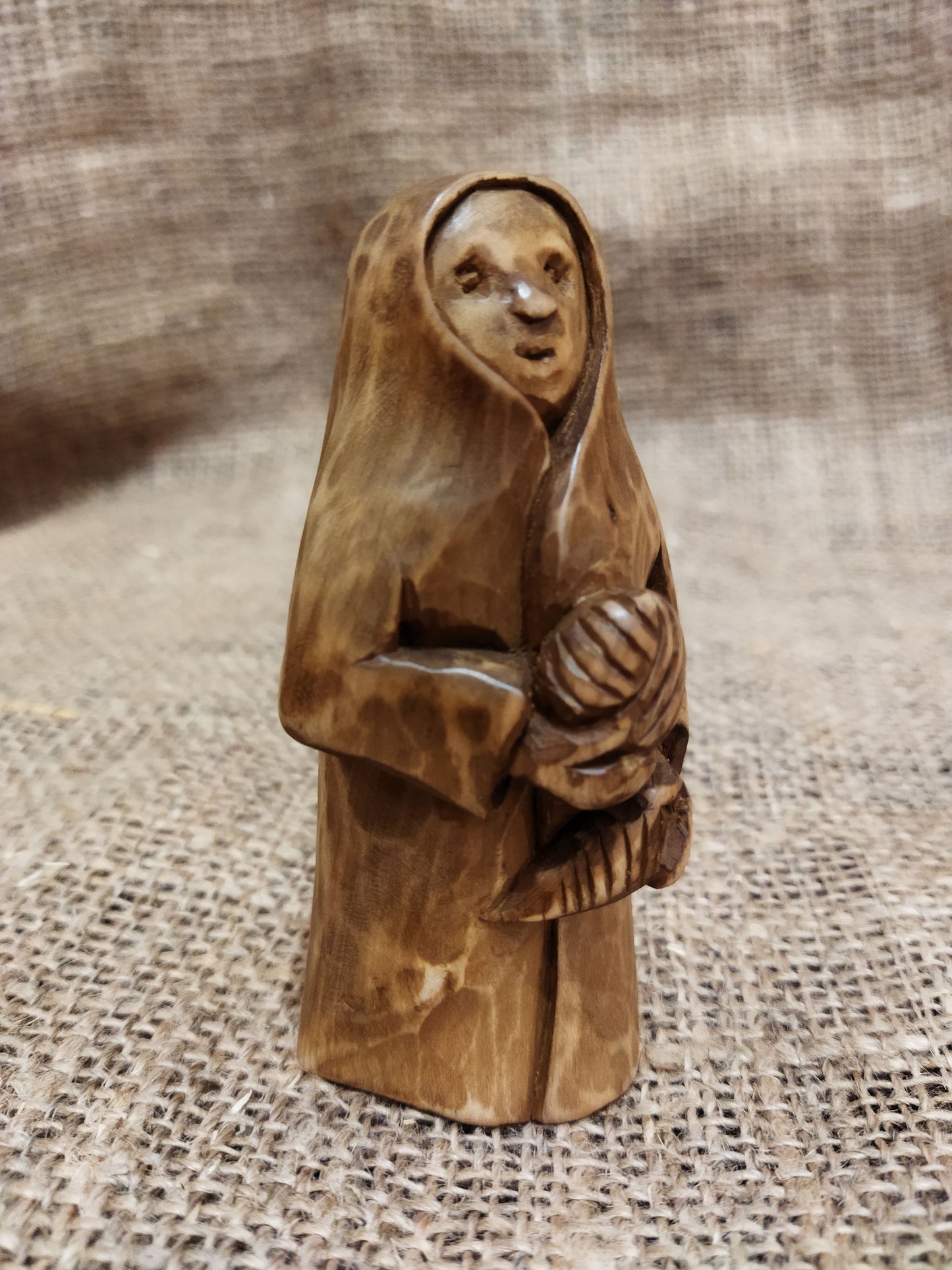 Hand-carved wooden statuette of the Slavic goddess Makosh, depicted with a serene expression, holding symbols of fate and abundance, set against a natural burlap background.