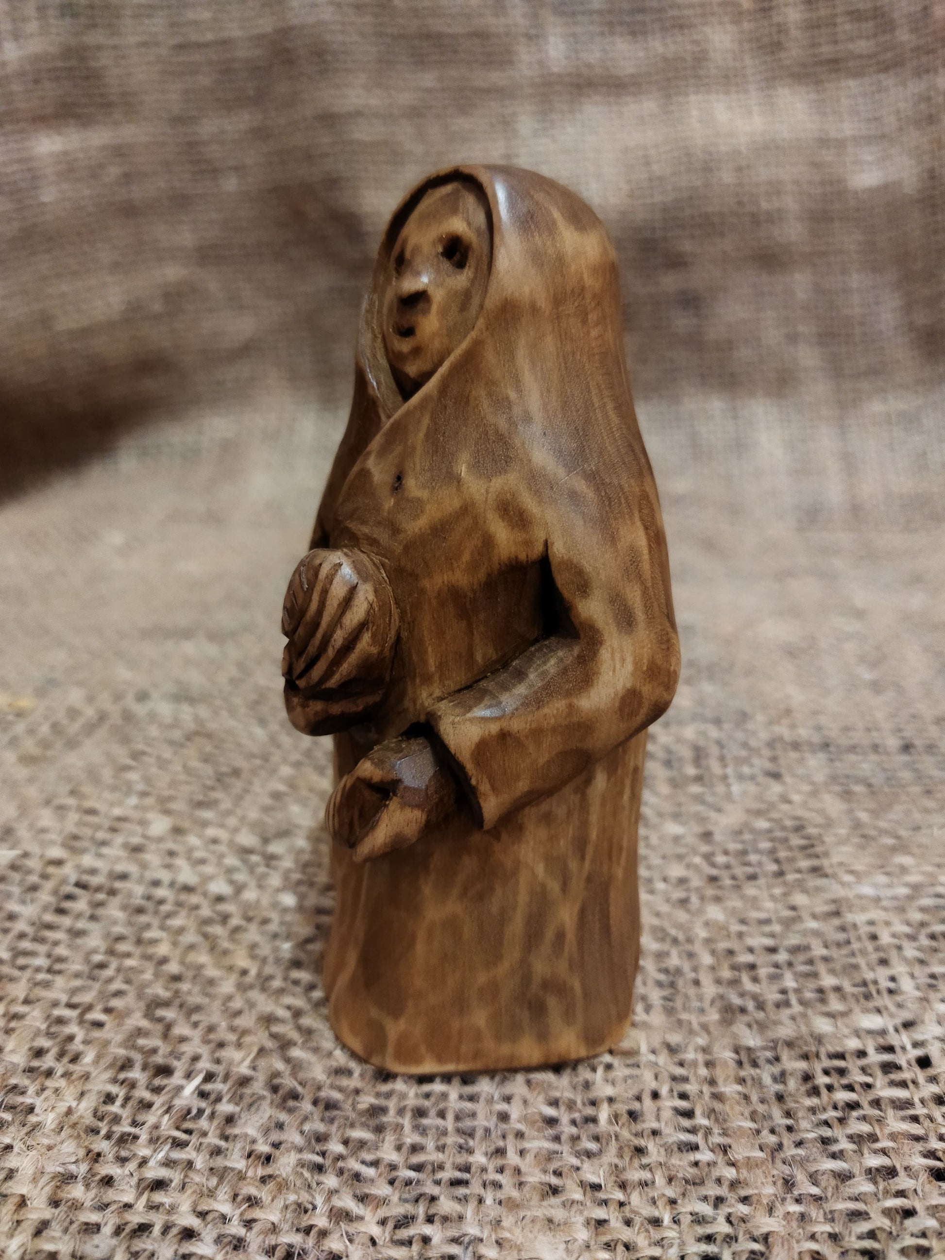 Hand-carved wooden statuette of the Slavic goddess Makosh, depicted with a serene expression, holding symbols of fate and abundance, set against a natural burlap background.