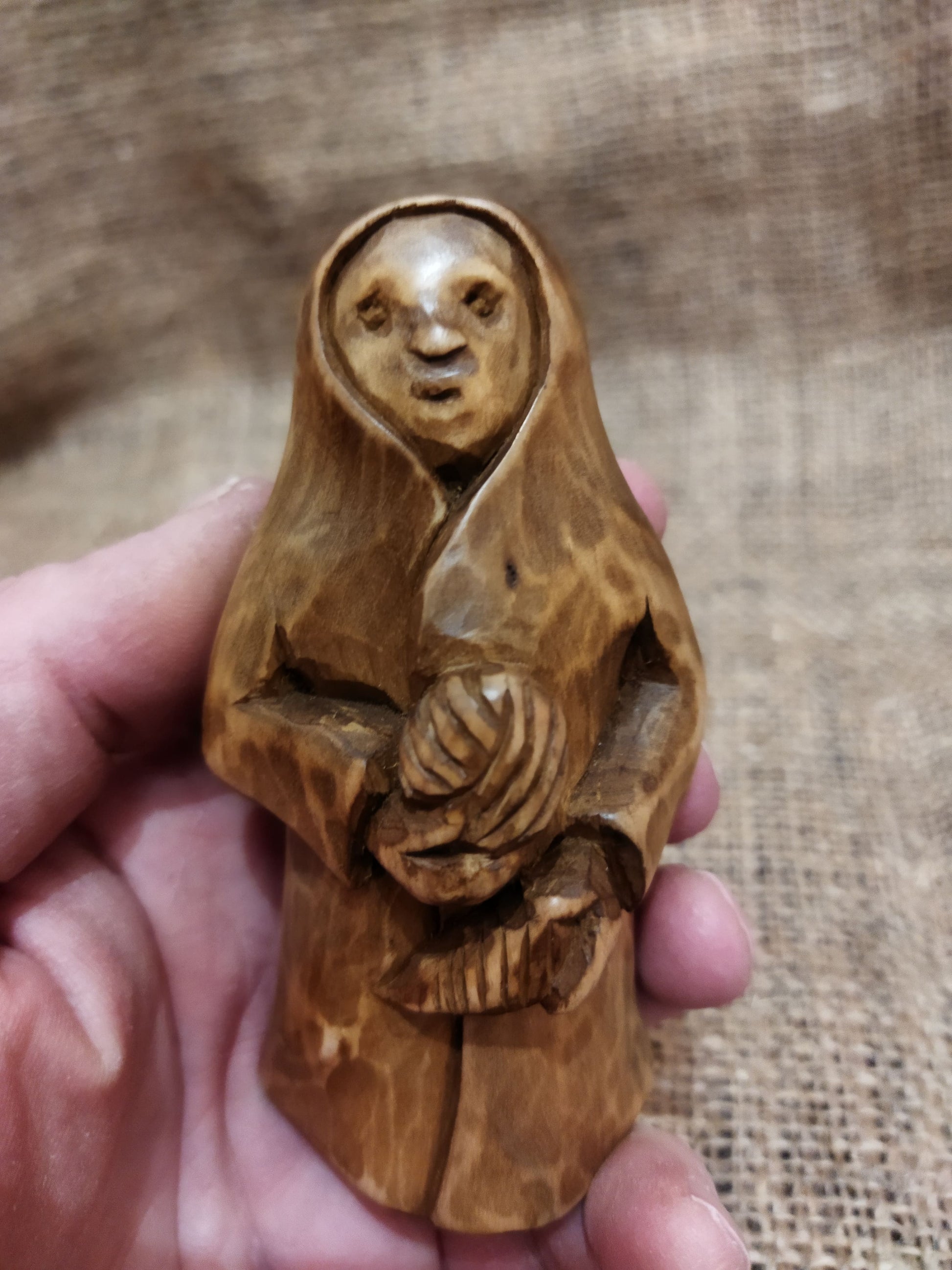 Hand-carved wooden statuette of the Slavic goddess Makosh, depicted with a serene expression, holding symbols of fate and abundance, set against a natural burlap background.