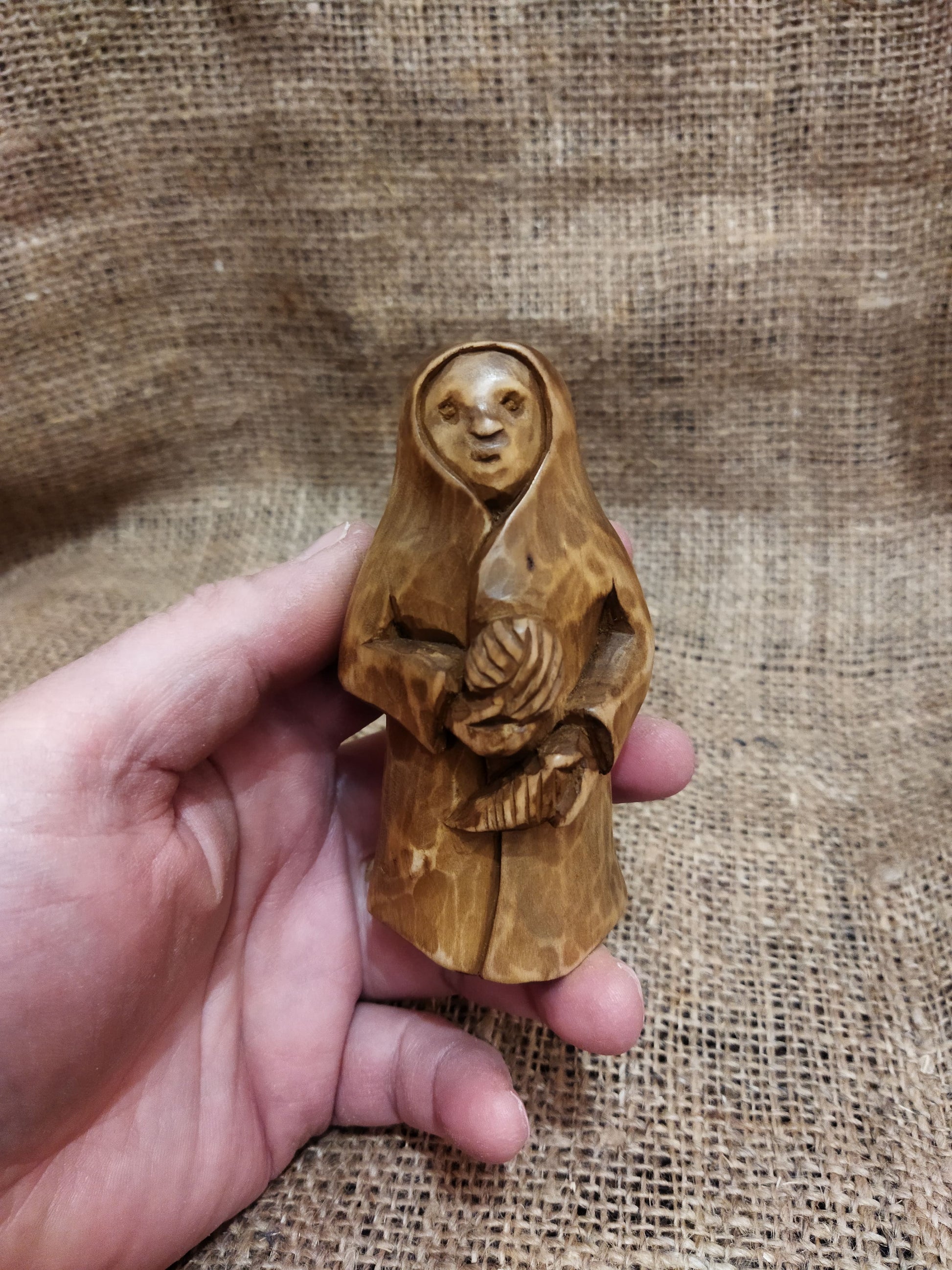 Hand-carved wooden statuette of the Slavic goddess Makosh, depicted with a serene expression, holding symbols of fate and abundance, set against a natural burlap background.