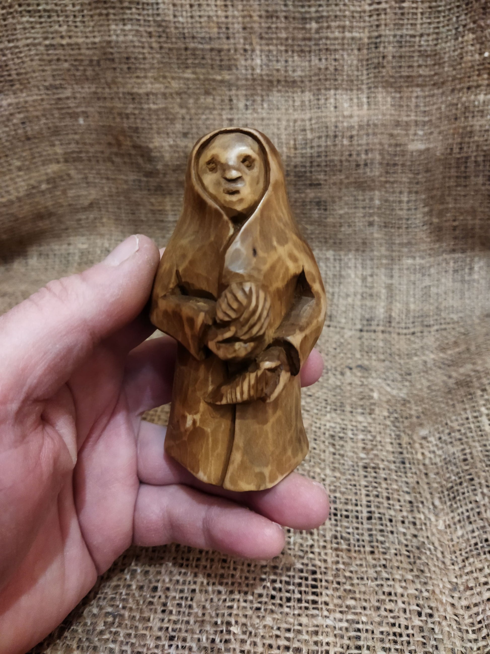 Hand-carved wooden statuette of the Slavic goddess Makosh, depicted with a serene expression, holding symbols of fate and abundance, set against a natural burlap background.