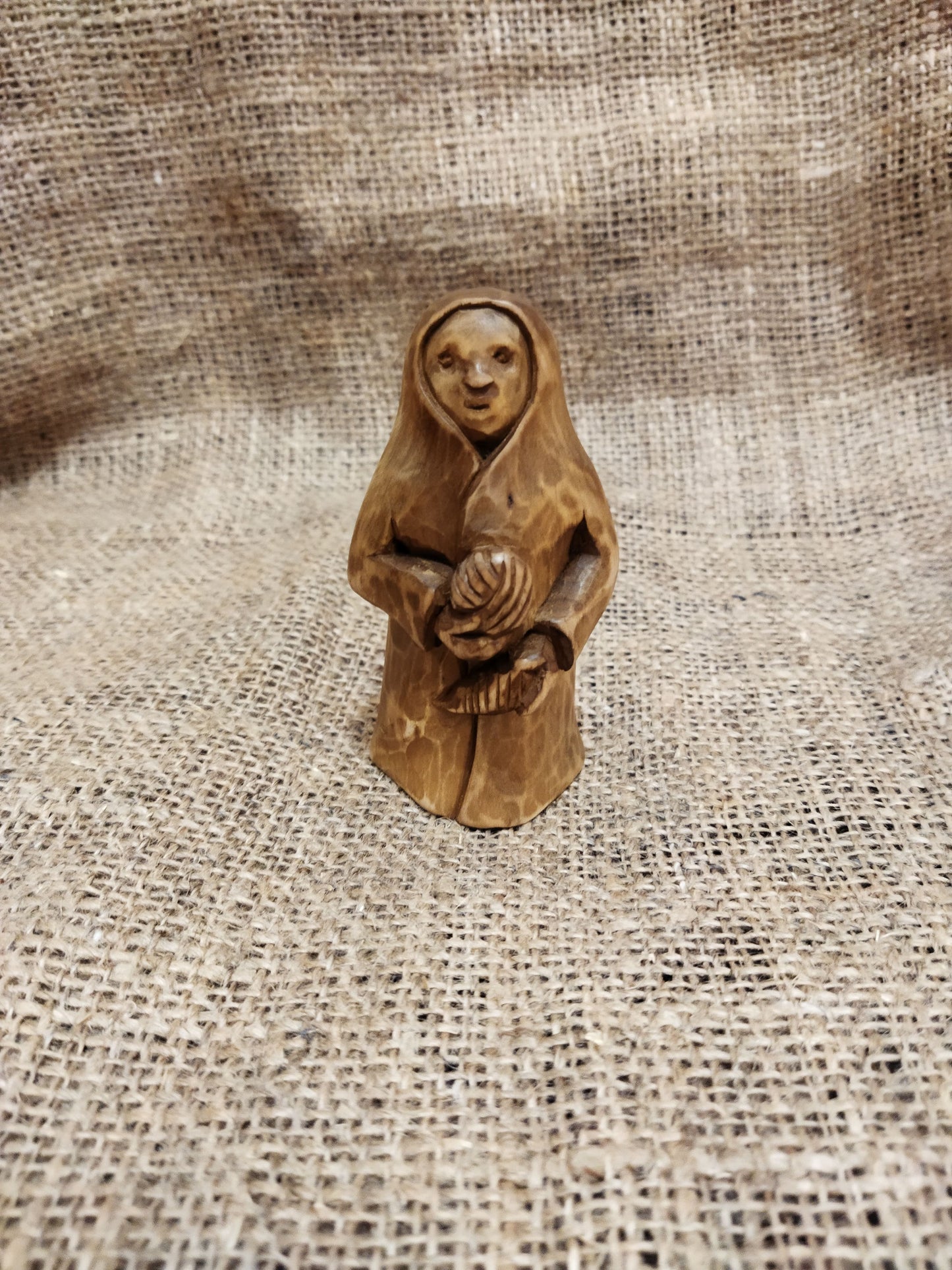 Hand-carved wooden statuette of the Slavic goddess Makosh, depicted with a serene expression, holding symbols of fate and abundance, set against a natural burlap background.