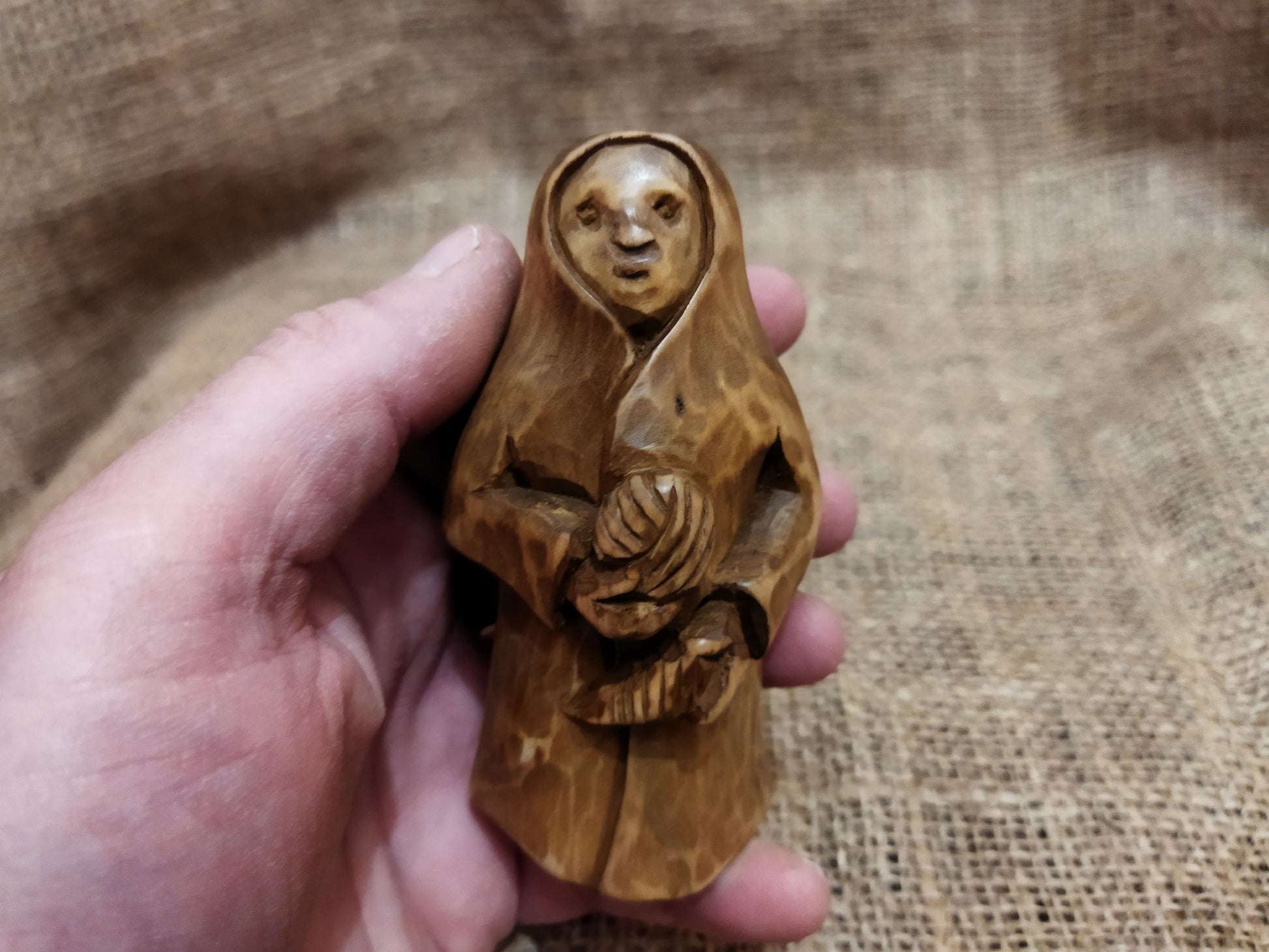 Hand-carved wooden statuette of the Slavic goddess Makosh, depicted with a serene expression, holding symbols of fate and abundance, set against a natural burlap background.