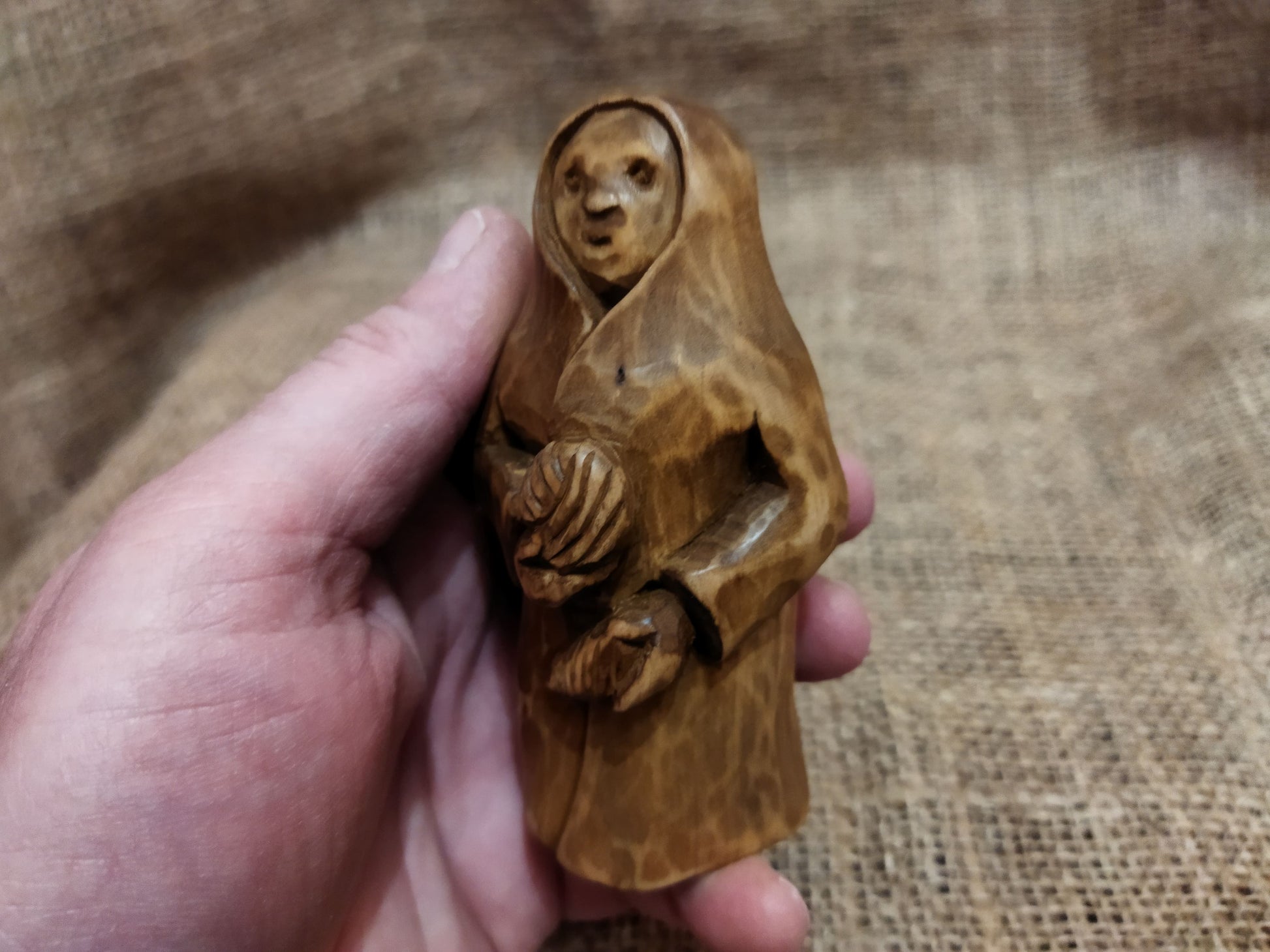 Hand-carved wooden statuette of the Slavic goddess Makosh, depicted with a serene expression, holding symbols of fate and abundance, set against a natural burlap background.