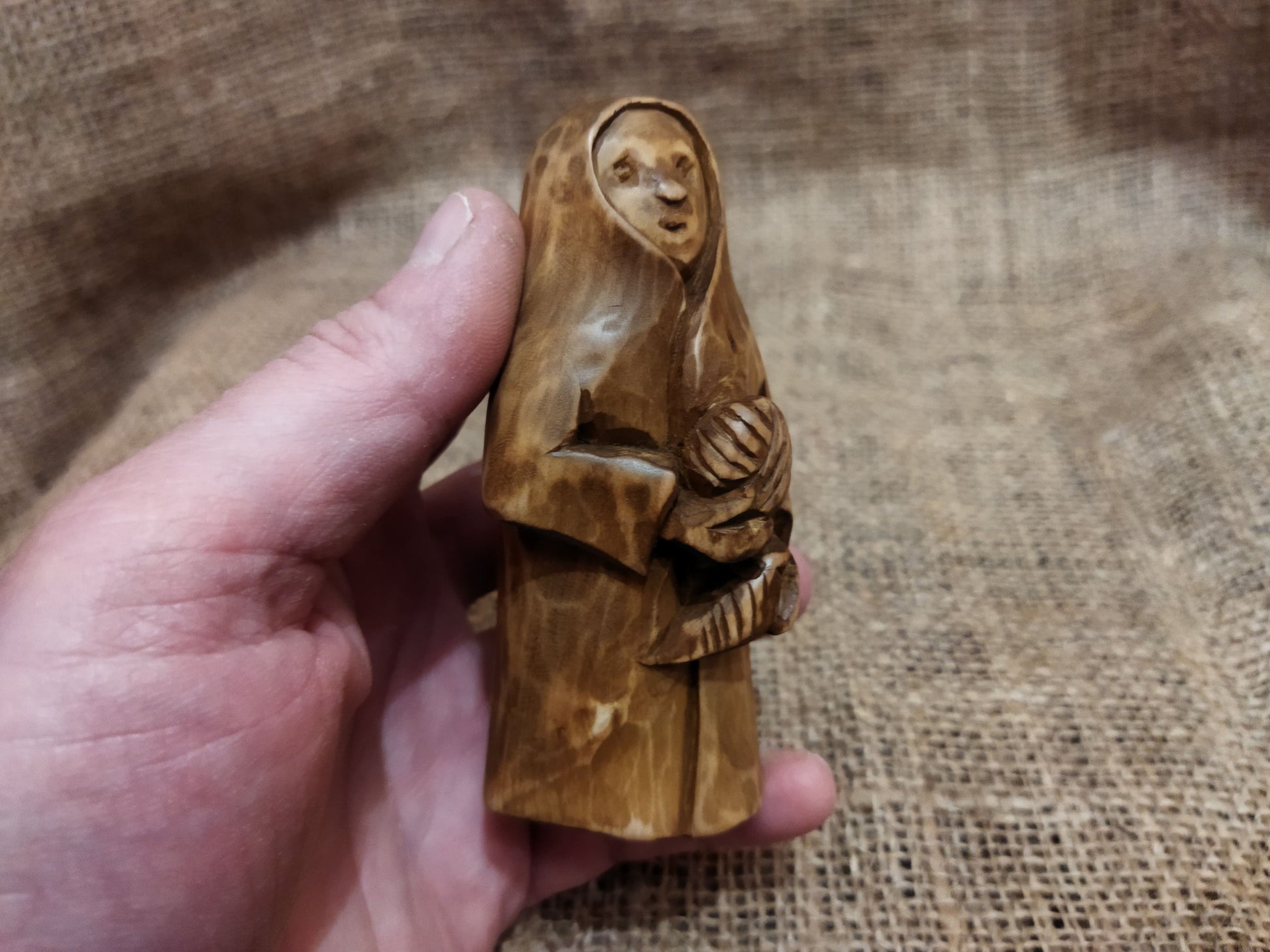 Hand-carved wooden statuette of the Slavic goddess Makosh, depicted with a serene expression, holding symbols of fate and abundance, set against a natural burlap background.