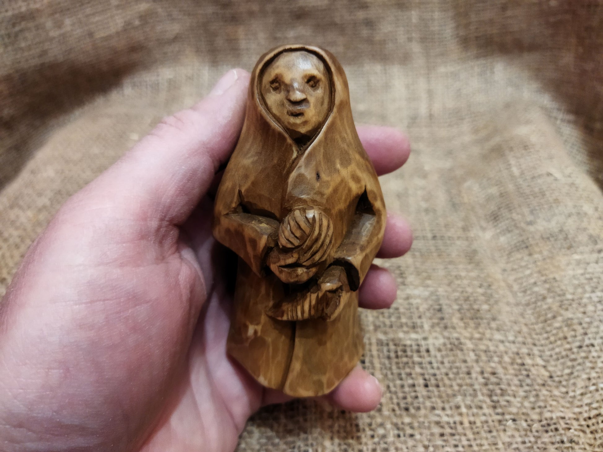 Hand-carved wooden statuette of the Slavic goddess Makosh, depicted with a serene expression, holding symbols of fate and abundance, set against a natural burlap background.