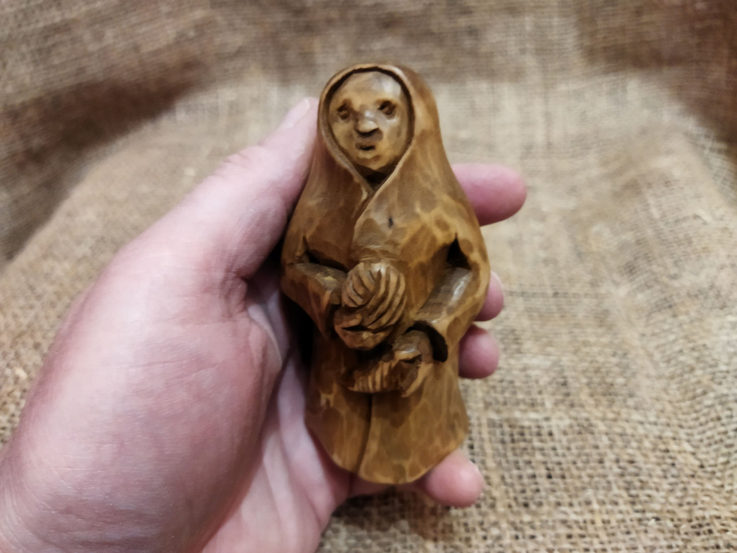 Hand-carved wooden statuette of the Slavic goddess Makosh, depicted with a serene expression, holding symbols of fate and abundance, set against a natural burlap background.